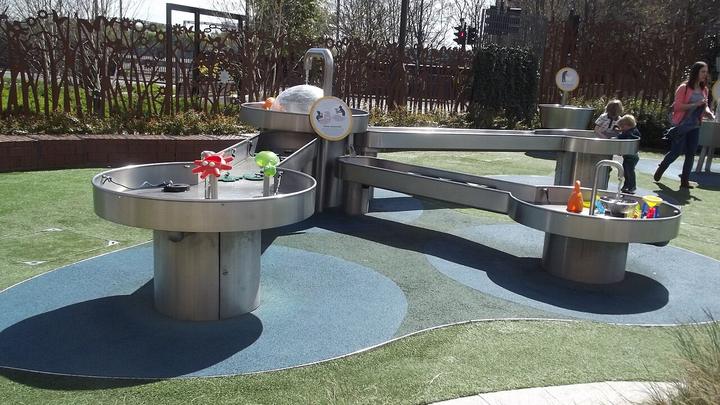 Children's play equipment set on open ground within a planted municipal park.